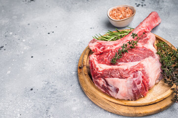Uncooked tomahawk steak, raw black angus beef rib eye with bone on wooden board. grey background. top view