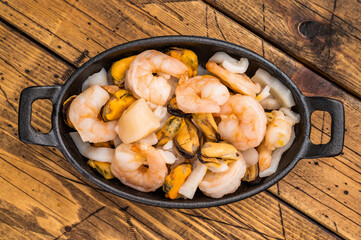 Ready for cooking fresh Raw Seafood Cocktail with Mussels, Clams, Prawns, Shrimps and squid in skillet. wooden background. top view