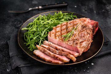 BBQ grilled pork tender steak, neck meat, on plate with salad. black background. top view