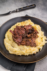 German Braised Beef Cheek, Slow cooked meat with smashed potatoes on a plate. grey background. top view