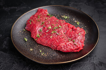 Marinated Flank or Flap steak, raw beef meat with thyme and spices on plate. black background. top view