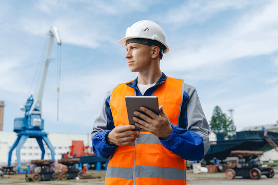 Male worker use internet tablet computer in shipyard with crane and cargo containers in background