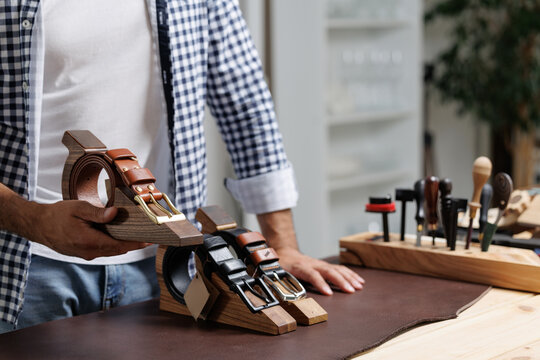 Male craftsman displaying handmade product leather belts in artisan workshop