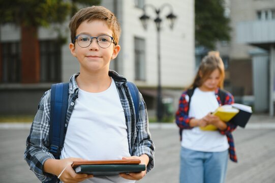 Back to school. Pupil of primary school on the way to study. Little first grader in glasses and with school bag. Beginning of lessons. First day of fall. Boy outdoors near school building