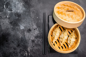 Steamed Korean Dumplings with pork meat and vegetables in bamboo steamer. black background. top view