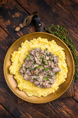 Beef Stroganoff over mashed potatoes with creamy sauce in a plate. wooden background. top view