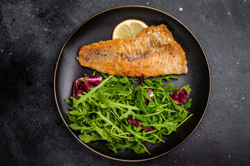 Roasted Haddock fish fillet on a plate with salad. black background. top view