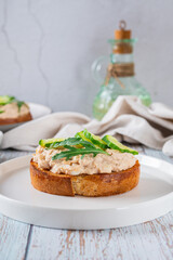 Cod liver, cucumber slices and arugula crostini on a plate on a table vertical view