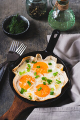 Fried eggs with green onions in a tortilla on a frying pan on the table vertical view
