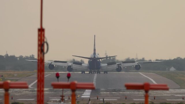 Huge four-engine aircraft braking after landing, slowing down, rear view. Wide-body airliner arrival