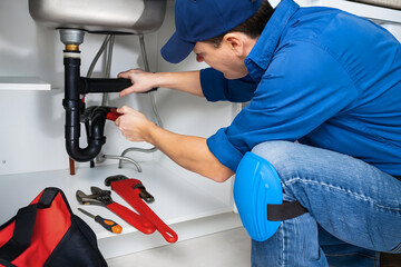 Professional plumber fixing under-sink drain with pipe wrench. Close-up of P-trap, pipes and tools. Home maintenance, leak repair, kitchen renovation, emergency plumbing service.