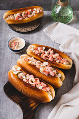 Grilled hot dogs with shrimps, tomatoes, eggs and sauce on a board on a table vertical view