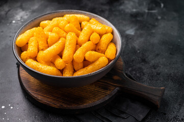 Deliciously addictive cheese flavored corn puffs, beautifully arranged on a plate. black background. top view