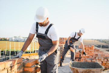 A team of Indian construction workers in overalls and hard hats are building a brick wall