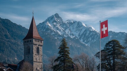 Swiss flag flies proudly beside a historic tower with a pointed roof, set against a backdrop of majestic snow-capped mountains and lush green slopes