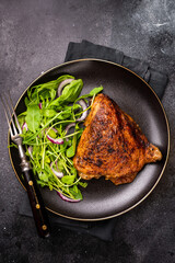 Roasted chicken thigh with salad on a plate, poultry meat. black background. top view