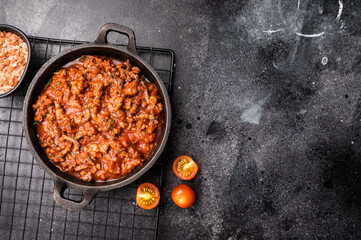 Bolognese sauce with minced beef, tomato paste and herbs in a skillet. black background. top view