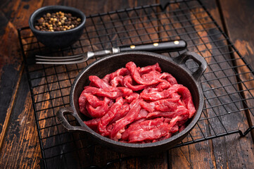 Raw beef meat sliced strips for beef stroganoff in a skillet. wooden background. top view