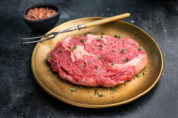 Raw Rib eye steak with herbs and spice in plate, fresh beef meat. black background. top view