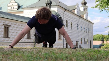 Man trains outdoors doing one arm push up on grass near historic building showing strength focus and determination combining modern fitness with cultural architecture and urban lifestyle