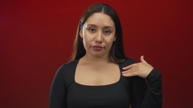 Young hispanic woman wearing a fitted black long sleeve top with palm raised and eyes closed against a red studio wall; indifference.