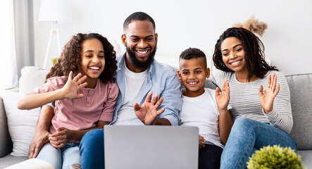 Online Communication. Smiling african american man, woman boy and girl making digital video call with friends or grandparents using laptop, waving to webcam, sitting on the couch in living room