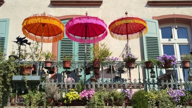 Balcony decorated with colorful flowers potted plants and three bright parasol umbrellas in European town on sunny day