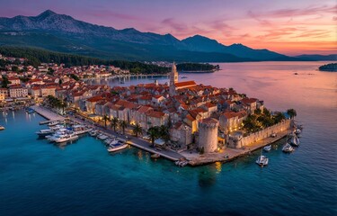 Fototapeta premium A stunning sunset casts a warm glow over a coastal town with boats anchored in the calm waters and mountains in the background