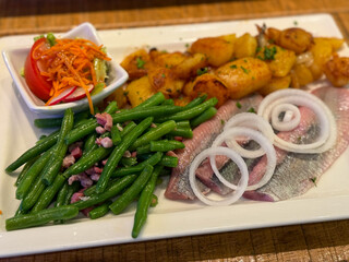 Traditional north german dish with marinated herring matjes filet, onion rings, roasted potatoes and green salad on the plate high angle view