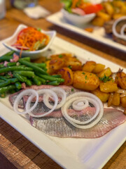 Traditional north german dish with marinated herring matjes filet, onion rings, roasted potatoes and green salad on the plate high angle view