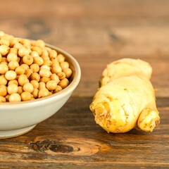 Light-colored bowl of soybeans next to a piece of ginger on a wooden surface