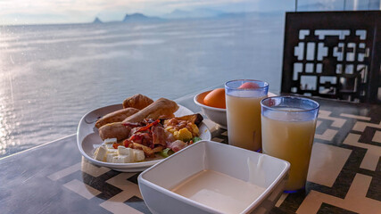 Breakfast with ocean view. Plate of breakfast with juice and fruit served on table overlooking calm ocean view.
