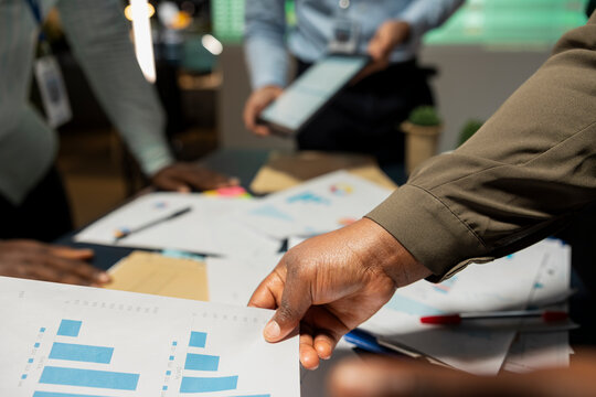 Close up of diverse project team shares analytics reports during advisory board event after hours, reviewing business intel and preparing insight for upcoming presentation with associates.
