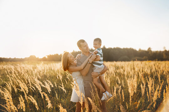 A family is having a joyful time outdoors as the sun sets. The parents are playing with their son in a tall grass field, creating cherished memories under the warm light.