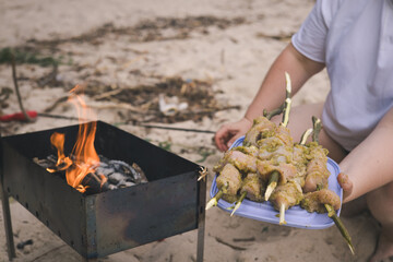 Preparing marinated chicken skewers over a charcoal grill on the beach A person prepares marinated chicken skewers for grilling over a charcoal fire on the beach, setting up for a summer cookout.
