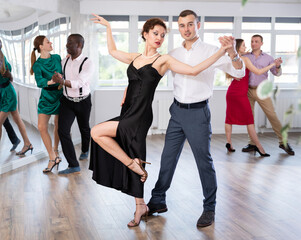 Fototapeta premium Dynamic young male and female attendees of dancing courses doing waltz in group