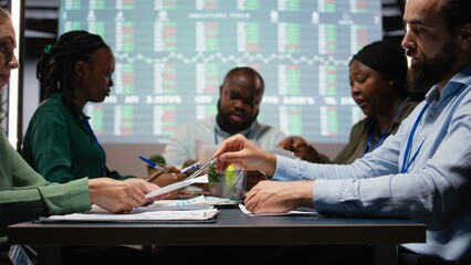 Multiethnic team reviewing infographics to offer solutions to fix project issues, working after hours to finish tasks before deadline. Analysts attending problem solving meeting. Camera A.