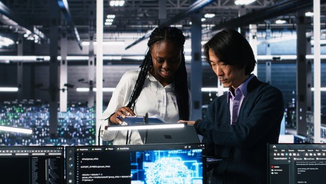 Team of data center engineers looking over paperwork and using deep learning algorithms to analyze datasets. Employees in multiethnic server farm using AI to recognize data patterns, camera A