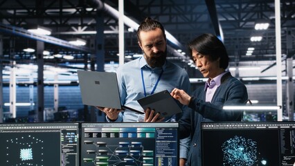 Data center manager supervising developer using device to monitor neural network AI LLMs. Team leader checking progress done by worker overseeing servers powering machine learning processes, camera A