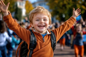 A happy little boy student with a beaming smile raises both hands in joy outdoors, welcoming the first day of school, new academic year, and the Day of Knowledge celebration.