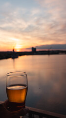 A chilled craft beer glass glistening in the golden hour light, overlooking a serene dock water view. Perfect for beverage branding, lifestyle content, and evoking relaxation, summer vibes, and premiu