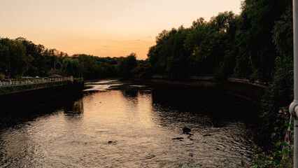 Fototapeta premium A breathtaking golden hour sunset with vibrant colors reflecting perfectly on the calm water near a historic lock and dam. This peaceful scene embodies tranquility and the beauty of nature's cycles.