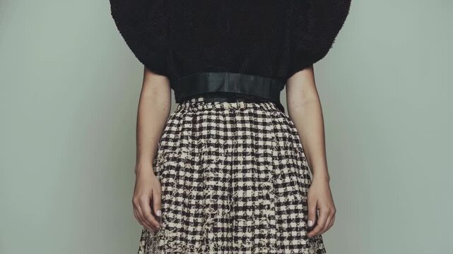 Woman in avant-garde black top and gingham skirt against mint background. Fashion video showcasing contrast of voluminous sleeves and fitted waist. Retro-modern style concept.