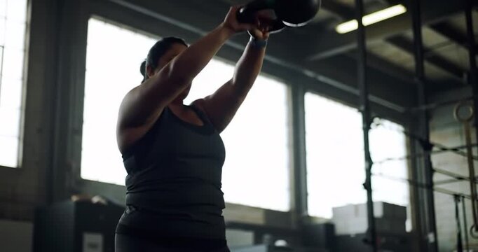 Powerful curvy woman performing an explosive kettlebell swing in a gym