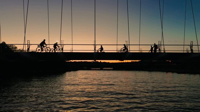 Cyclists and pedestrians cross the Humber River Bridge against a summer sunset