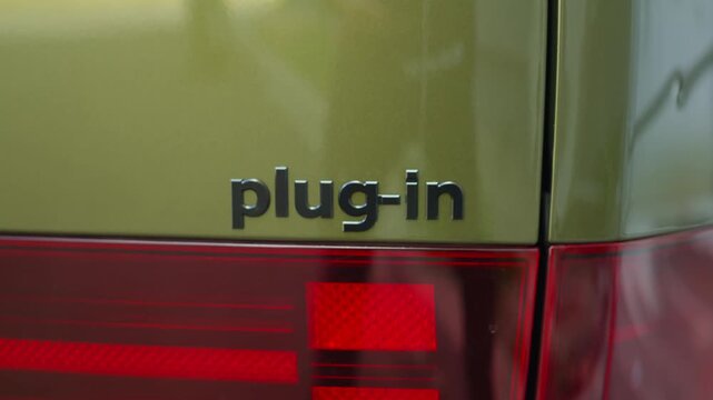 Close up shot of plug in electric vehicle with rechargeable battery packs charged from electric grid. PEV automobile logo on green car, extreme closeup handheld camera shot