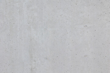 Fototapeta premium Close-up texture of a raw concrete wall. The surface shows natural imperfections, small holes, and subtle variations in color, typical of unfinished or industrial-style concrete.