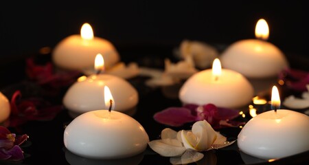 Burning candles and orchid flowers floating in water on black background, closeup