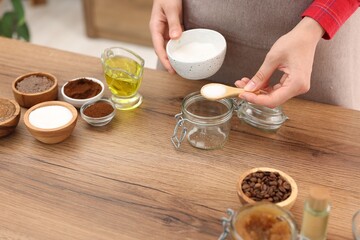 Making natural scrub. Woman adding sugar into jar at wooden table, closeup