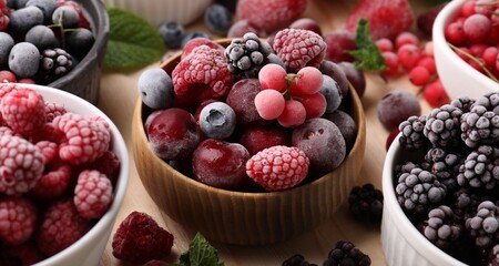 Different ripe frozen berries and mint leaves on light wooden table, closeup